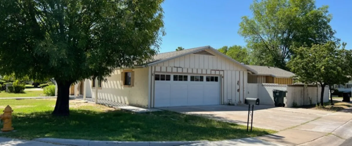 Single-story home with attached garage, driveway, and large shade tree in front yard.