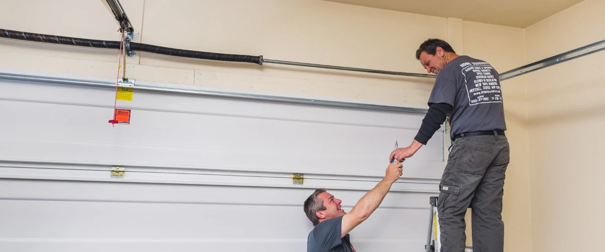 Garage door technicians working together to install and secure a residential garage door panel. Garage door technicians working together to install and secure a residential garage door panel.