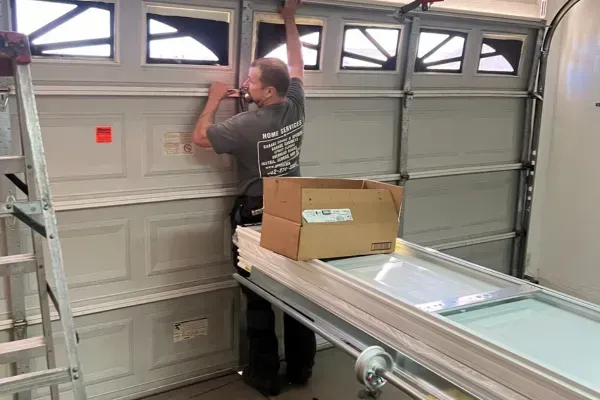 Technician installing garage door panel with box and new panel on stand