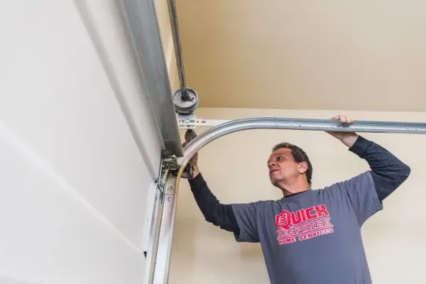 Professional technician repairing a garage door track and hardware inside a residential garage.