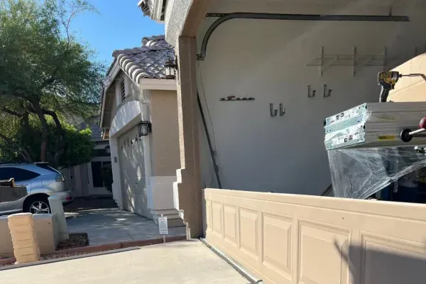 A panoramic view of a garage interior with a worker on a ladder installing a garage door opener above new door panels on sawhorses.
