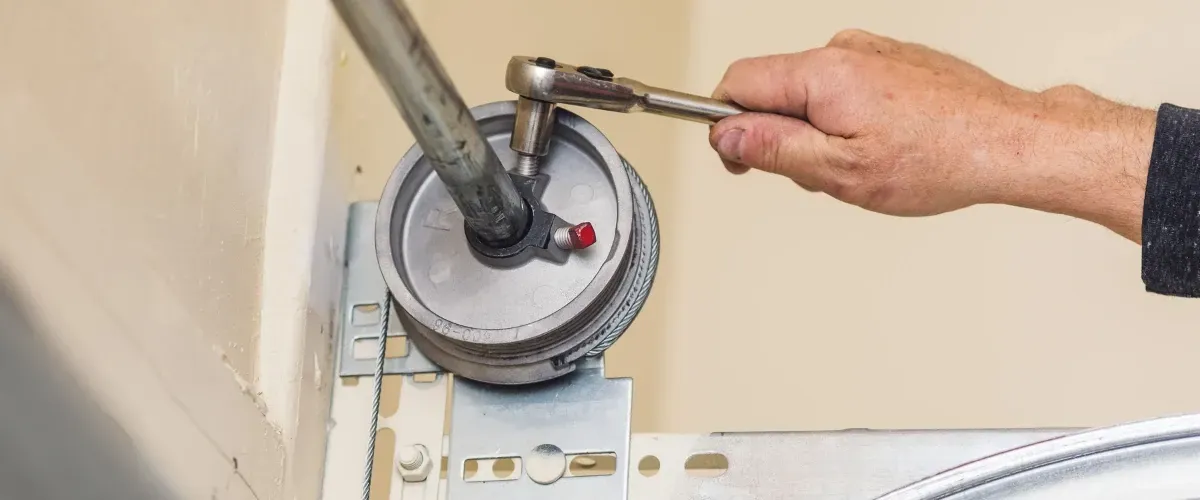 Technician tightening a garage door torsion spring bracket using a ratchet wrench.