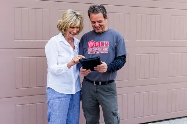 Garage door service technician reviewing repair details with a homeowner using a tablet in front of a residential garage.